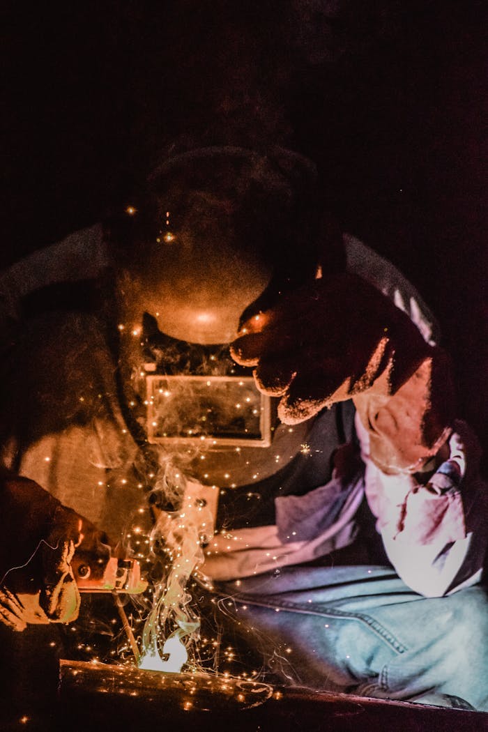 A welder in protective gear works amid sparks in a visually striking, low-light setting.