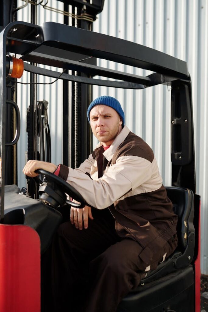 Man operating forklift in warehouse environment wearing blue beanie.